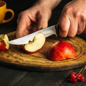 Someone using a knife to cut an apple